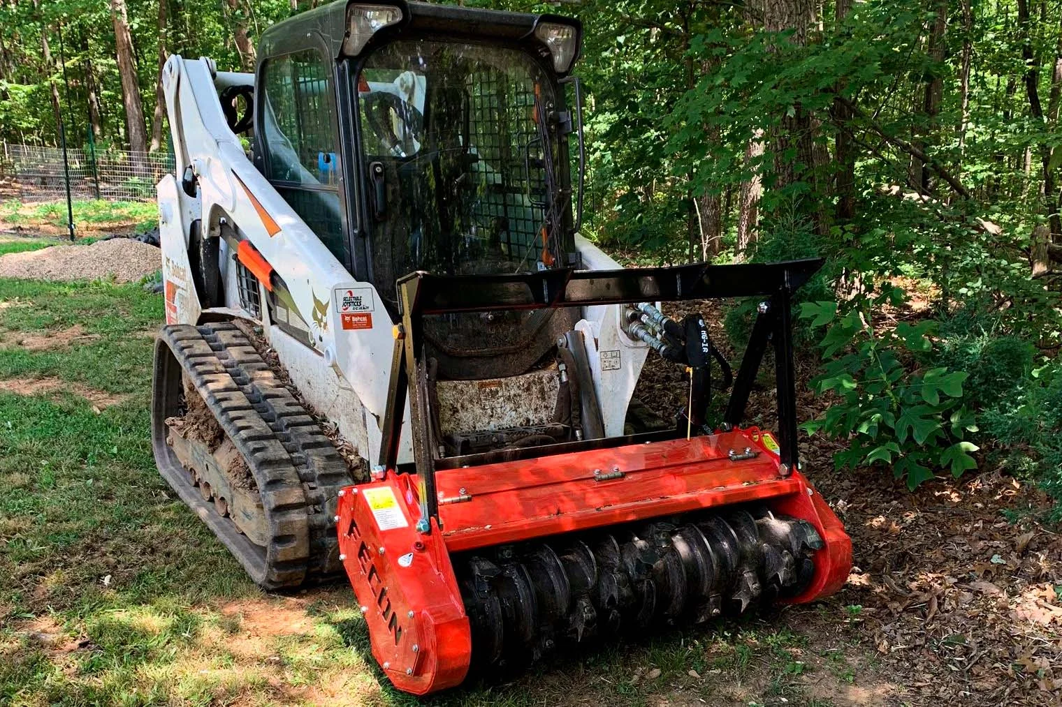 Tracked loader with a forestry mulcher beside overgrown woodland